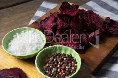 Dried beetroot with bowl of salt and black pepper on chopping board