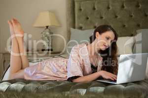 Beautiful bride using laptop while relaxing on bed