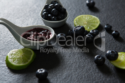 Slice of lemon and spoon with blueberries on black background