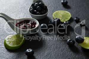 Slice of lemon and spoon with blueberries on black background