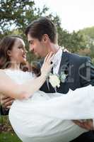 Bridegroom carrying bride while standing in park