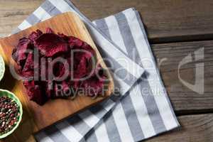 Dried beetroot with bowl of black pepper on chopping board