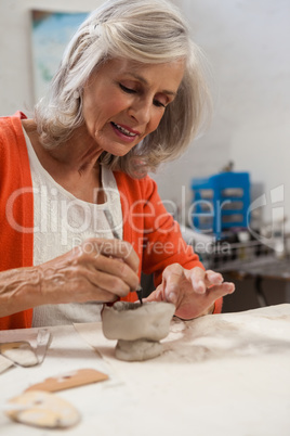Attentive senior woman shaping a clay pot