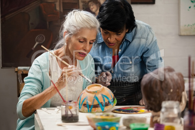 Woman assisting senior woman in painting bowl at drawing class