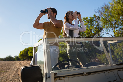 Young couple looking through binoculars at forest