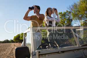 Young couple looking through binoculars at forest