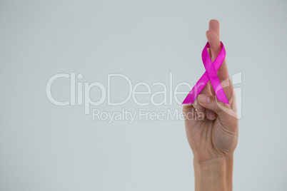 Cropped hand showing crossed fingers with pink ribbon