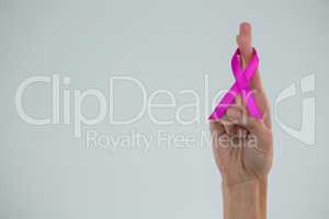 Cropped hand showing crossed fingers with pink ribbon