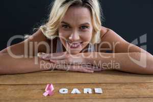 Portrait of smiling woman leaning on table with pink ribbon and care text