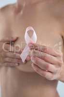 Close up of woman covering breast while showing pink ribbon