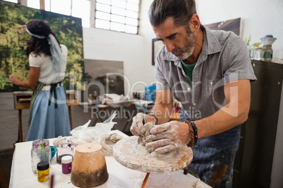 Man molding clay while woman painting on canvas