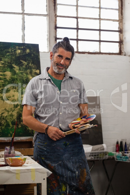 Portrait of confident man standing with palette and paintbrushes