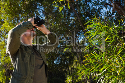 Man looking through binocular by tree
