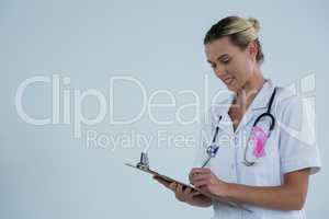 Female doctor with pink ribbon writing on clipboard