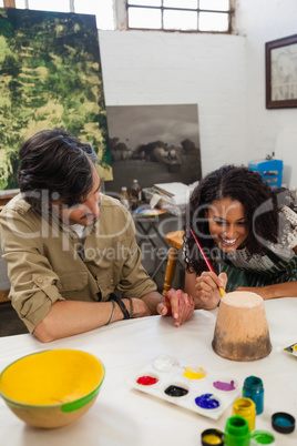 Man assisting woman in painting vase