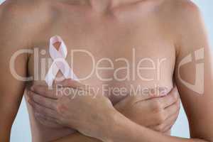 Mid section of woman with  Breast Cancer Awareness ribbon covering breast