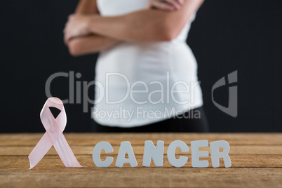 Mid section of woman with arms crossed by table with pink ribbon and cancer text