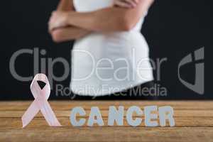 Mid section of woman with arms crossed by table with pink ribbon and cancer text