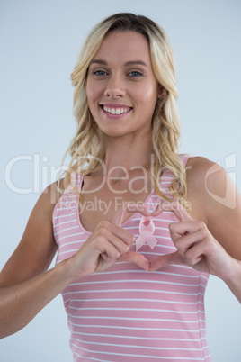 Smiling woman making heart shape on pink ribbon