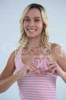 Smiling woman making heart shape on pink ribbon