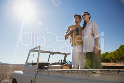 Couple looking away while standing in off road vehicle on landscape