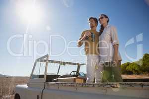 Couple looking away while standing in off road vehicle on landscape