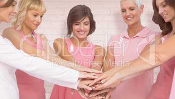 Composite image of female friends stacking hands for breast cancer awareness
