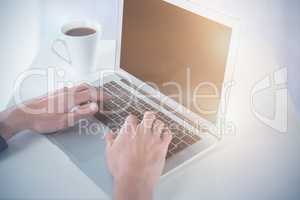 Composite image of cropped hands of businessman using laptop while having coffee