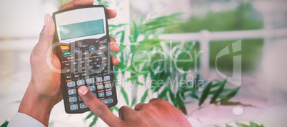 Composite image of cropped hands of businessman using calculator