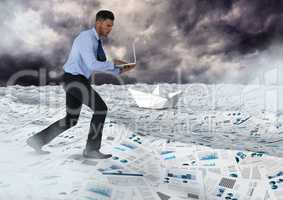 Businessman on laptop in sea of documents under sky clouds with paper boats
