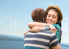 Millennial couple hugging against blurry coastline
