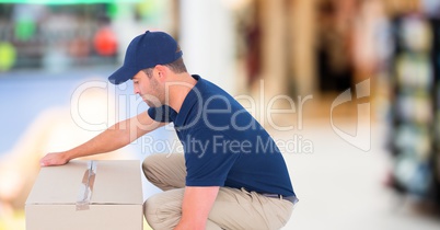 Delivery man picking up box against blurry shopping centre