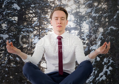 Business man meditating against snowy trees with sun shining through