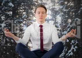 Business man meditating against snowy trees with sun shining through