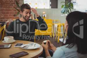 Woman giving ring to boyfriend at cafe