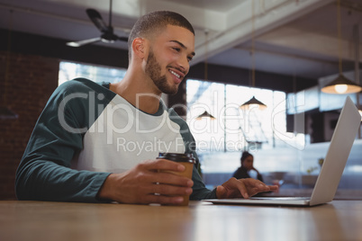 Man with coffee cup using laptop in cafe