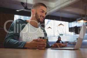 Man with coffee cup using laptop in cafe