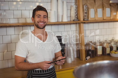 Portrait of smiling waiter holding tablet at cafe