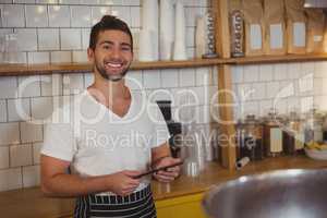Portrait of smiling waiter holding tablet at cafe
