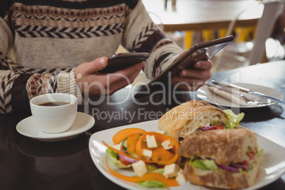 Mid section of man with breakfast using phone and tablet in cafe