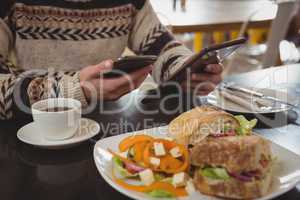 Mid section of man with breakfast using phone and tablet in cafe