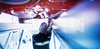 Mechanic girl watching under a car with a light