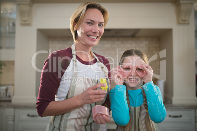 Daughter holding cookie cutter on her eyes and mother standing beside her