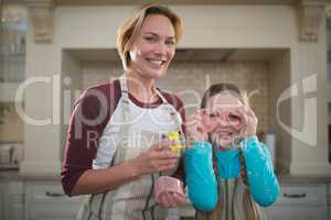 Daughter holding cookie cutter on her eyes and mother standing beside her