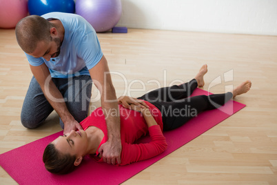 Instructor guiding female student in exercising at yoga studio