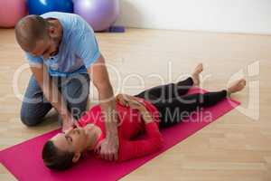 Instructor guiding female student in exercising at yoga studio