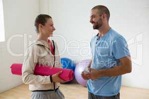 Student holding exercise mat talking to instructor in yoga studio