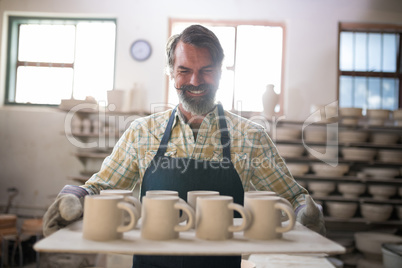 Happy male potter holding ceramic cups in tray