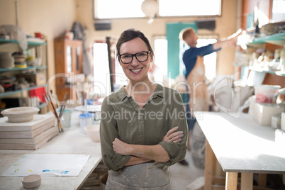 Female potter standing with arms crossed in pottery workshop