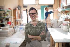 Female potter standing with arms crossed in pottery workshop